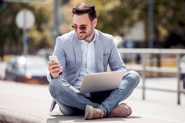 Wall Mural - Young attractive man sitting outside ,using cell phone