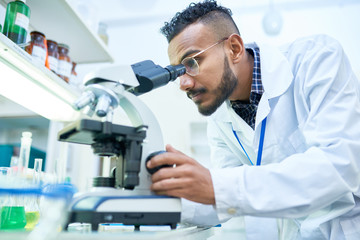 side view portrait of young middle-eastern scientist looking in microscope while working on medical 