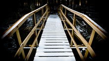 Snowy Wooden Footbridge Over Water. Artistic Wintry Scene With The Small Bridge In A Dark Forest. The Way Direct Forward.