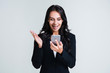 © MARIIA - Amazing news. Beautiful young businesswoman using her smartphone with smile while standing against white background