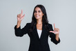 © MARIIA - One simple touch for technology. Beautiful young businesswoman pointing away and looking with smile while standing against white background