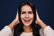 © MARIIA - So loud. Portrait of beautiful young woman making face and covering her ears while standing against black background