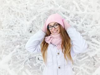 Wall Mural - Adorable happy young blonde woman in pink knitted hat scarf mittens having fun snowy winter park forest sunny day in nature