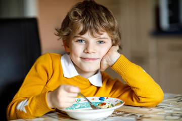 Adorable little school boy eating vegetable soup indoor.