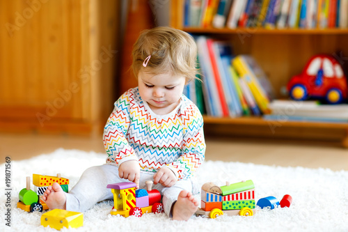 Fototapeta Adorable cute beautiful little baby girl playing with educational wooden toys at home or nursery. Toddler with colorful train