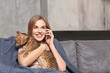 Beautiful young woman caressing cat and talking on mobile phone at home