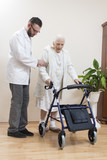 Fototapeta  - 2.	Staruszka uczy się chodzić przy pomocy balkonika rehabilitacyjnego  przy asekuracji lekarza.