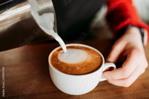 Plakat Barista przygotowuje ciepłą piankę do kawy cappuccino w białym szklanym kubku