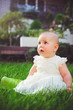 © lanarusfoto - half-year-old child sitting on the grass in the yard, dressed in a white dress rejoices, 6 months. Concept education of children, children's goods