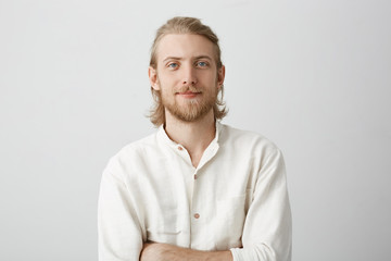 Portrait of positive handsome blond man with beard and moustache, standing with crossed hands in white shirt with slight smile and confident expression. Boyfriend picking flowers for his couple