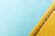 close-up of seamded up fabrics in two pastel tones - yellow and light blue with grey seam - visible weave - trendy decorative background with copy space for text