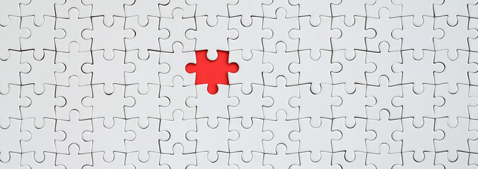 the texture of a white jigsaw puzzle in an assembled state with one missing element forming a red sp