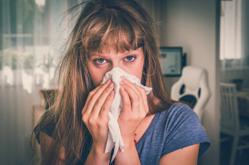 sick woman with flu or cold sneezing into handkerchief