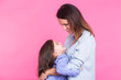 people, happiness, love, family and motherhood concept - happy little daughter hugging and kissing her mother over pink background