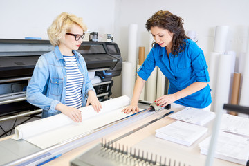 Fototapete - Portrait of two modern young women working in printing shop or publishing company, loading machines with paper and cutting brochures