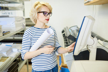 Fototapete - Portrait of blonde young woman using plotter machine operating it via computer while working in modern printing shop, copy space