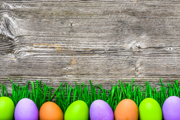 Wall Mural - Green grass and eggs, painted easter eggs on wooden background