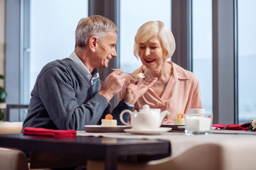 Adorable moment. Attractive pleasant mature man wedding his wife with desert white sitting at the table and grinning