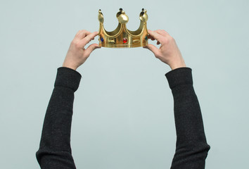 Hands are wearing a golden crown on head copy space isolated on light blue background. Winner. Leader. Selfish person. Award ceremony concept.