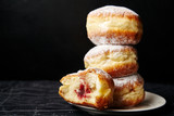 Fototapeta  - A stack of three sufganiyot donuts with jelly on black background