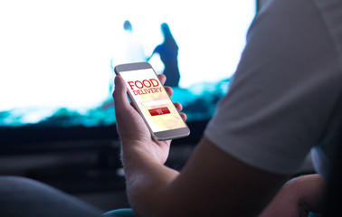 Take away food order online with delivery app and smartphone. Man buying pizza or fast food home while watching TV.