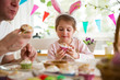 Father and daughter celebrating Easter, eating cupcakes covered with glaze. Happy family holiday. Cute little girl in bunny ears. Beautifully decorated room