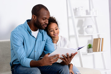 Wall Mural - african american father reading book to daughter at home