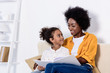 © LIGHTFIELD STUDIOS - african american mother and daughter looking at each other on sofa at home