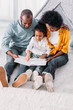 © LIGHTFIELD STUDIOS - african american daughter reading for parents on floor at home