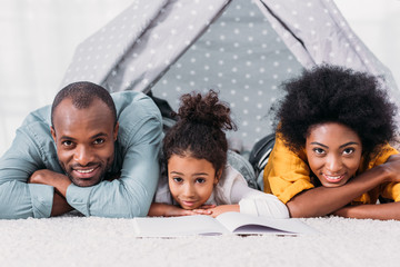 Wall Mural - african american parents and daughter lying on floor and looking at camera at home