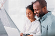 © LIGHTFIELD STUDIOS - side view of happy african american father and daughter using laptop at home