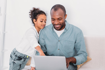 Wall Mural - african american daughter showing something on laptop to father at home