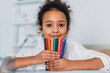 © LIGHTFIELD STUDIOS - adorable african american kid holding colored felt pens and looking at camera at home