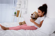 © LIGHTFIELD STUDIOS - adorable african american kid reading book and hugging teddy bear on bed