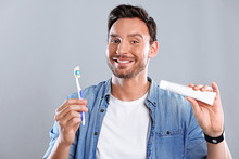 Handsome Bearded Man  With Healthy Teeth Isolated On A White Background. Guy Holding A Toothpaste And A Toothbrush Smiling