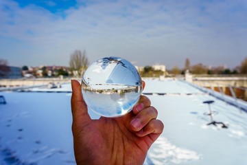 A hand holding crystal ball,  an orbuculum, is a crystal or glass ball and fortune telling object. With a blue sky during winter in Paris, France. Used also for optical sciences. 