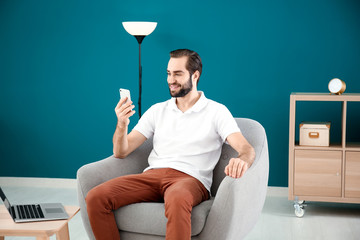 Canvas Print - Handsome man with mobile phone sitting in comfortable armchair at home