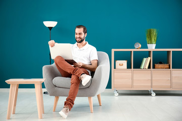 Sticker - Handsome man with laptop sitting in comfortable armchair at home