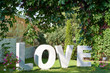 Big white letters Love on green grass in the garden outdoors, free space. Wedding decorations, romantic holiday decor. Love sign at wedding reception. Valentines day background. Love concept