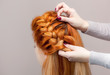 Beautiful, with long, red-haired hairy girl, hairdresser weaves a  braid, close-up in a beauty salon. Professional hair care and creating hairstyles.