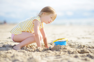 cute little girl having fun on a sandy beach on warm and sunny summer day. kid playing by the ocean.