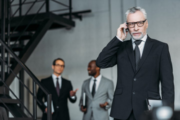 Wall Mural - selective focus of businessman talking on smartphone with colleagues behind in office