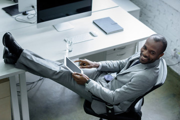 Wall Mural - smiling african american businessman with tablet at workplace in office