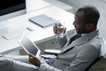 Wall Mural - african american businessman with glass of water using tablet at workplace in office