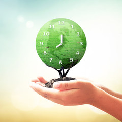 Poster - World environment day concept: Human hands holding clock of global grass tree on blurred nature background