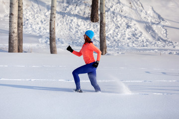 Wall Mural - Young woman in a bright blue hat, orange sweater  runnnig on a snow  on a bright winter day in forrest. Jogging in winter forest