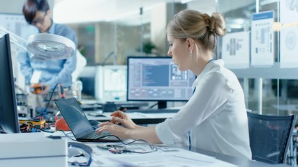 Wall Mural - Female Computer Scientists Connects Circuit Board to Her Laptop with Mock-up Green Screen. She Works in the Technologically Advanced Laboratory.