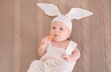 Poster - Cute little baby in bunny costume with carrot lying on plaid, top view