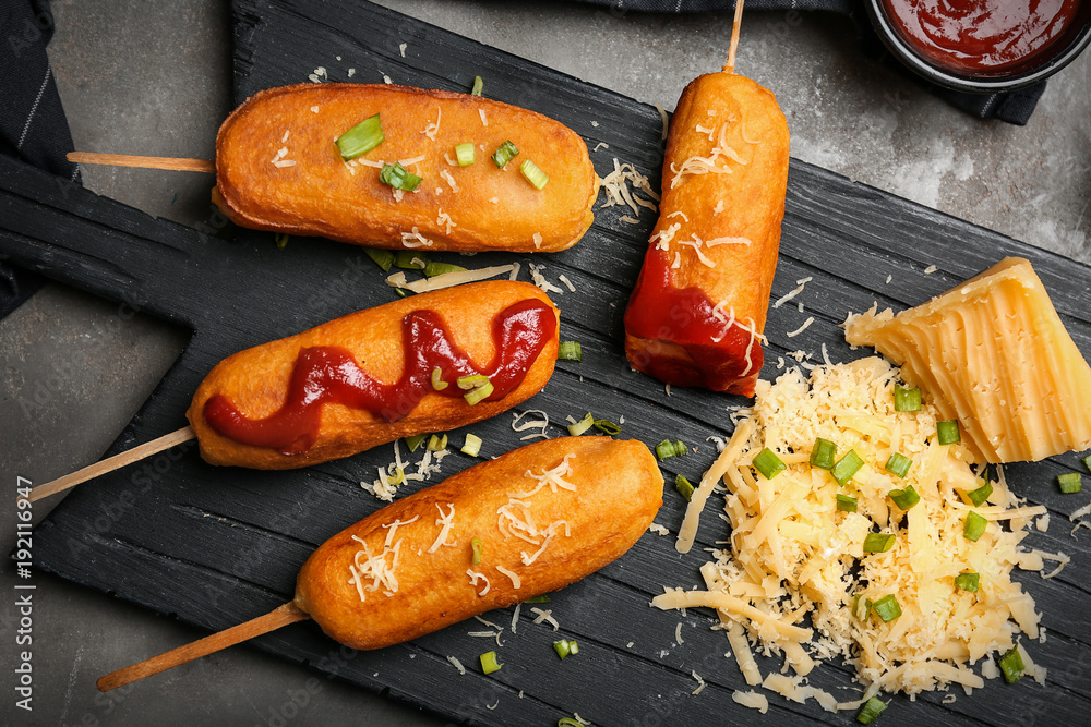 Tasty corn dogs with ketchup on wooden board