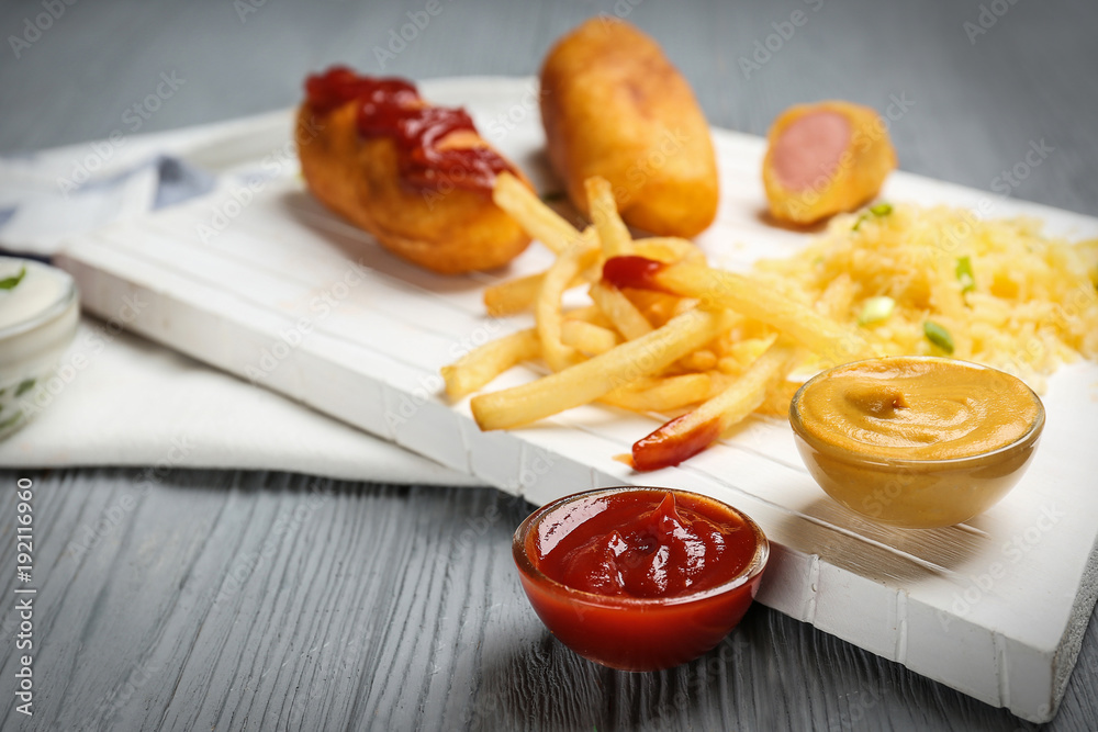Tasty corn dogs with sauces on wooden board